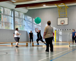Mehrere Personen spielen in einer Sporthalle mit einem großen Ball.