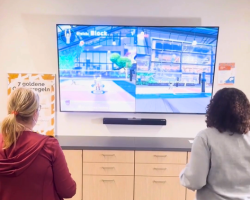 Zwei Frauen sitzen vor einem großen Bildschirm und halten Controller in den Händen.